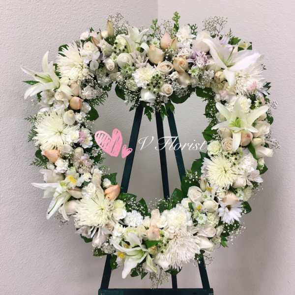Large white and pale peach floral wreath on a stand against a light wall