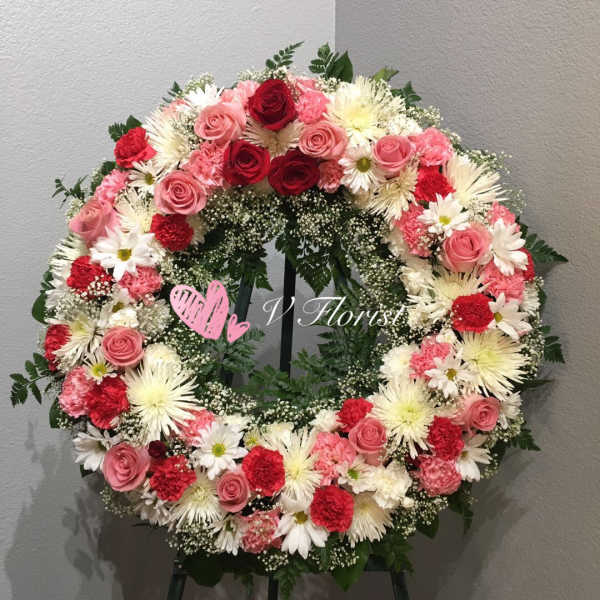 Standing wreath with pink and red roses, carnations, and white daisies on an easel
