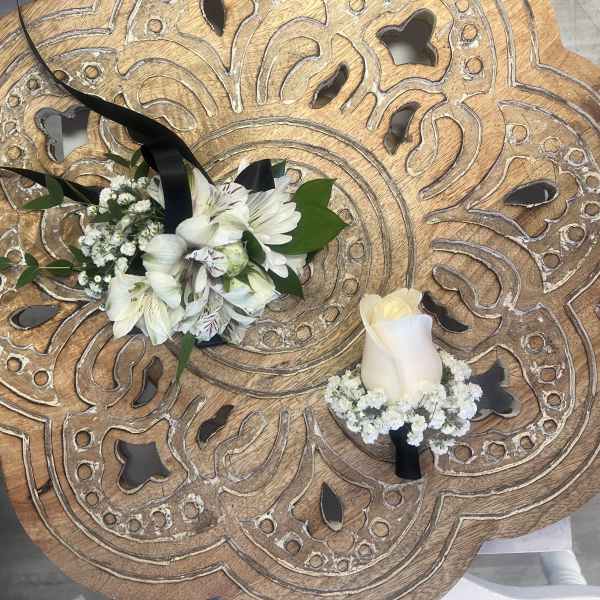 White floral corsage with black ribbon and matching white rose boutonniere on carved wooden table