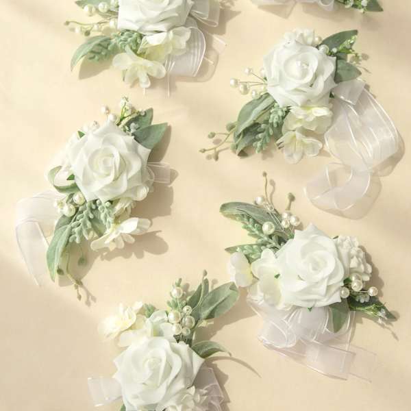 Set of white rose and pearl corsages with sheer white ribbon on a light beige background