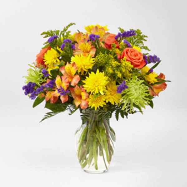Mixed bouquet of yellow, orange, and purple flowers in a glass vase