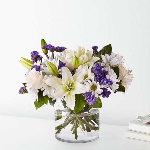 White lilies and daisies with purple filler in a clear glass vase