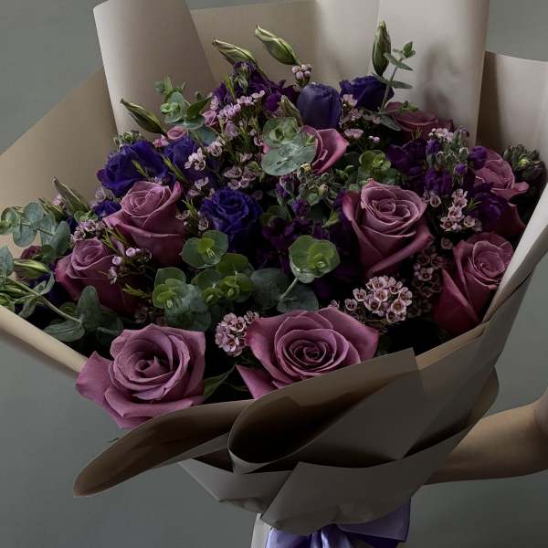 Bouquet of purple roses and small pink flowers wrapped in beige paper