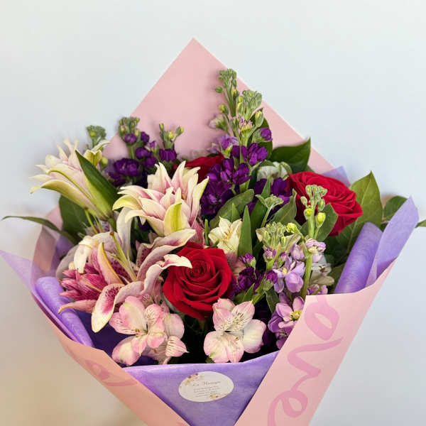 Bouquet of red roses and pink lilies wrapped in pink and purple paper