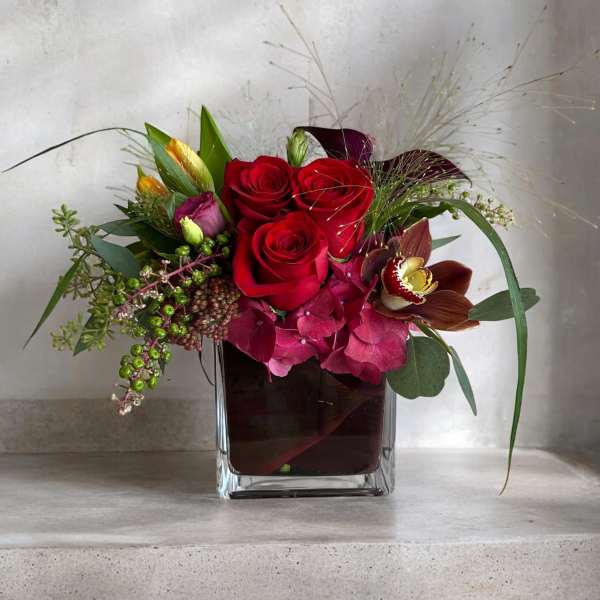 Red roses and pink orchids in a square glass vase