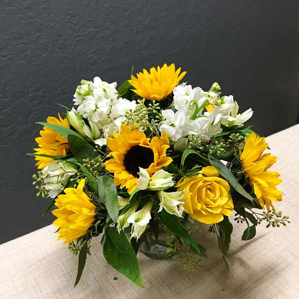Yellow sunflowers and roses arranged in a glass vase