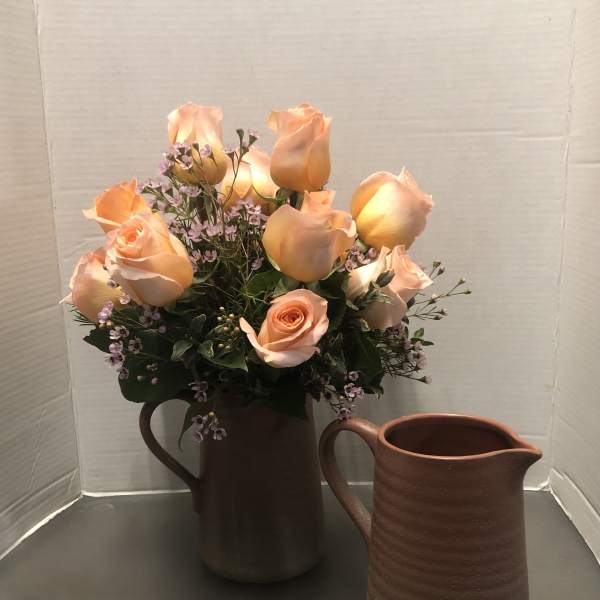 Peach roses arranged in a brown pitcher with a matching empty pitcher beside it.