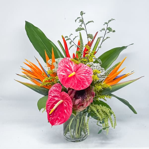 Tropical bouquet with pink anthuriums and orange bird-of-paradise in a glass vase