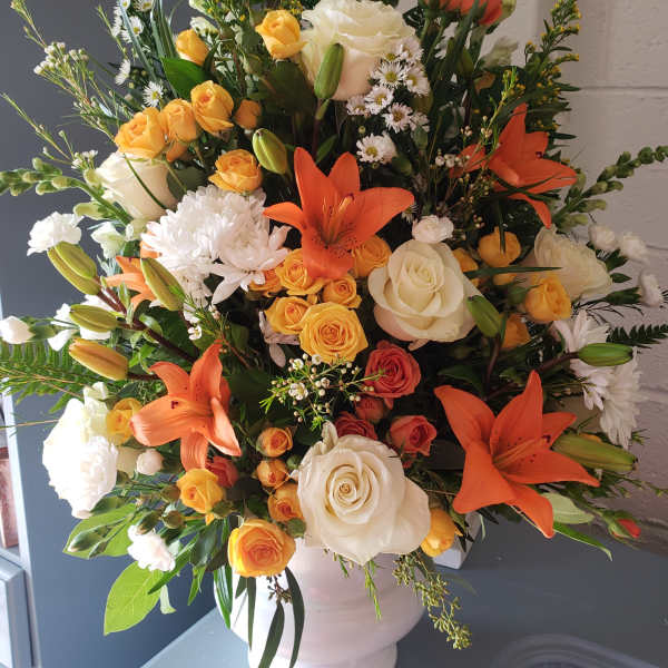 Large bouquet of orange lilies, white roses, and yellow spray roses in a white vase