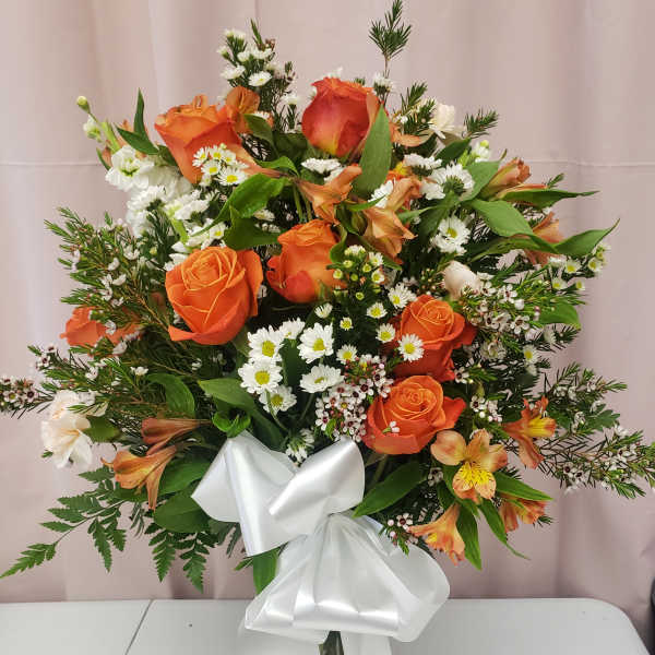 Orange roses and white daisies in a clear vase with a white ribbon