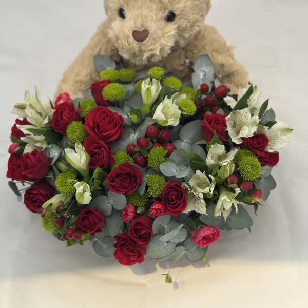 Teddy bear holding a bouquet of red roses and white flowers