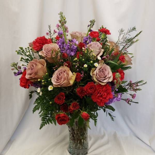 Mixed bouquet of roses, carnations, and purple flowers in a glass vase