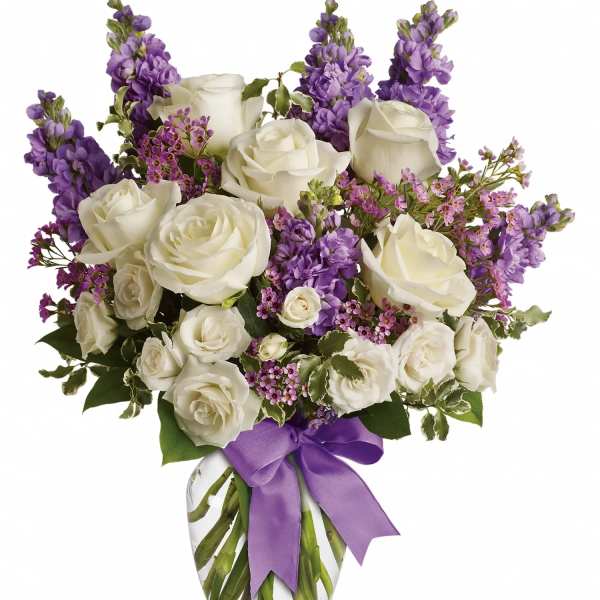 White roses and purple flowers in a glass vase with a purple ribbon