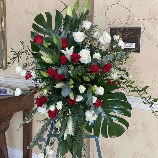 Standing floral spray with red and white roses and lilies on an easel