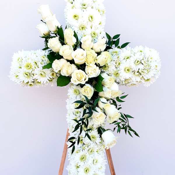 White floral cross with roses and daisies on a stand