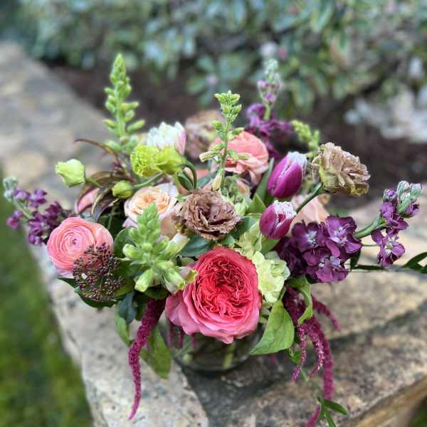 Mixed bouquet of pink, purple, and peach flowers in a glass vase