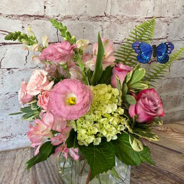 Pink mixed bouquet with green hydrangea and a blue butterfly pick in a clear glass cube vase