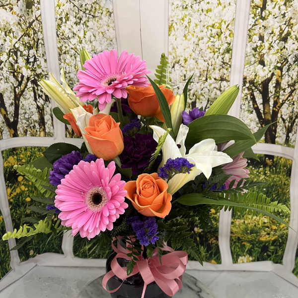 Bouquet of pink gerbera daisies, orange roses, and white lilies in a black vase