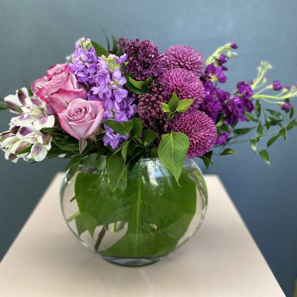 Pink and purple flowers arranged in a round glass vase