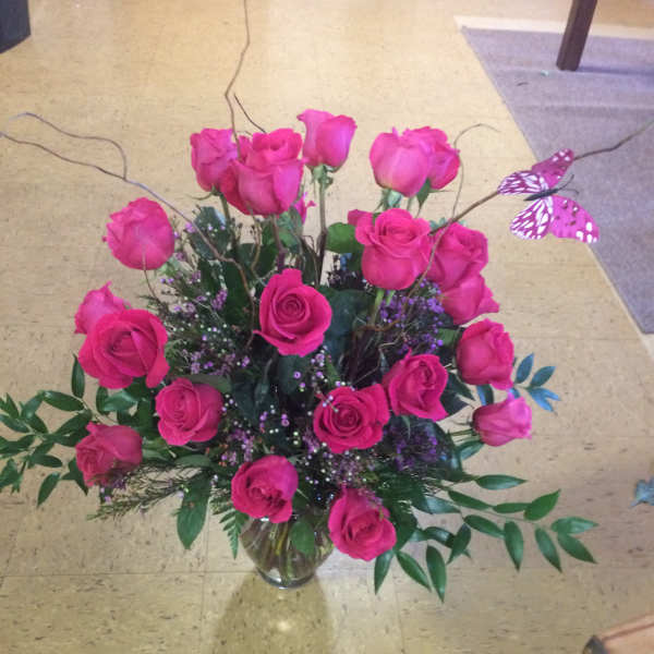 Tall arrangement of hot pink roses with curly branches and a pink butterfly in a clear glass vase