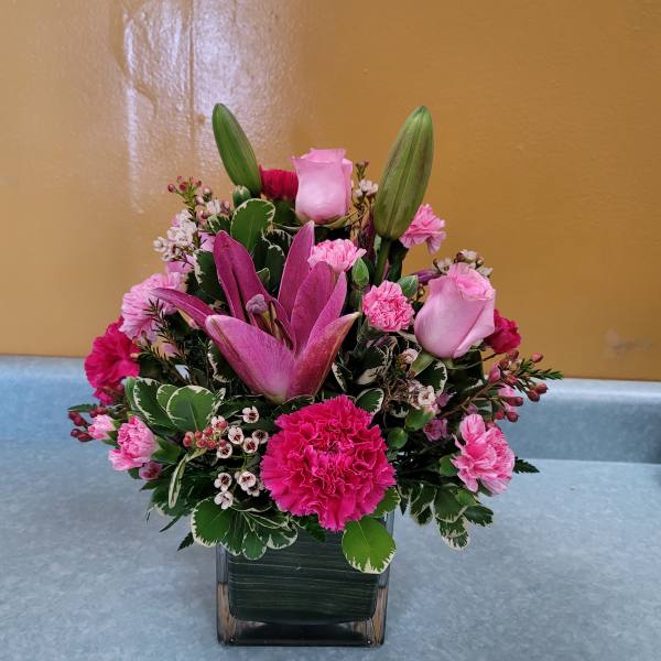 Pink lilies and roses arranged in a square glass vase