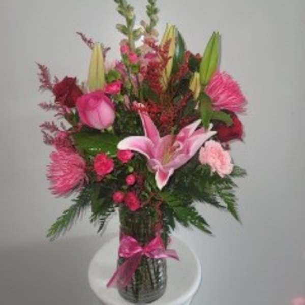 Pink and red floral arrangement in a glass vase with a pink ribbon
