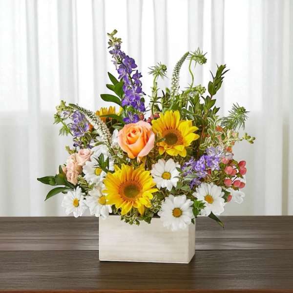Mixed bouquet in a white rectangular vase with sunflowers, roses, and daisies