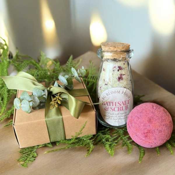 Gift box with ribbon, bath salt jar, and pink bath bomb on greenery