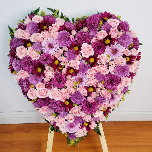 Heart-shaped floral arrangement of pink and purple blooms on an easel