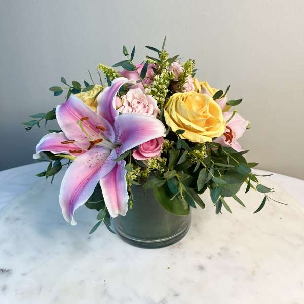 Pink lily and roses in a glass vase with greenery