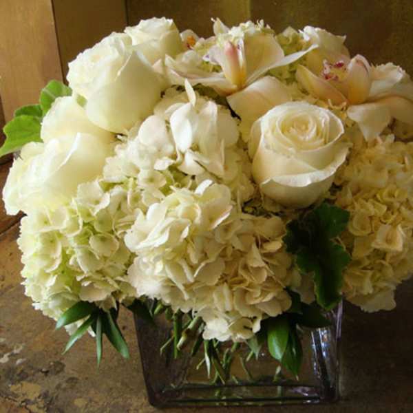 All white hydrangeas, roses and orchids in a clear square glass vase.