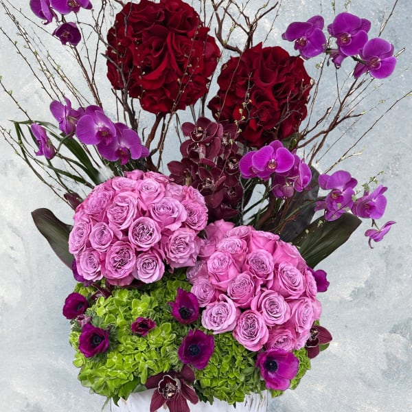 Pink and red floral arrangement in a white round box with orchids