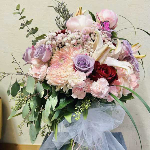 Bouquet of pink, lavender, and red flowers with white lilies and tulle ribbon