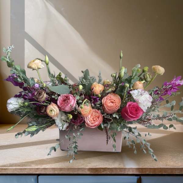 Low floral arrangement of pink and peach roses in a white container