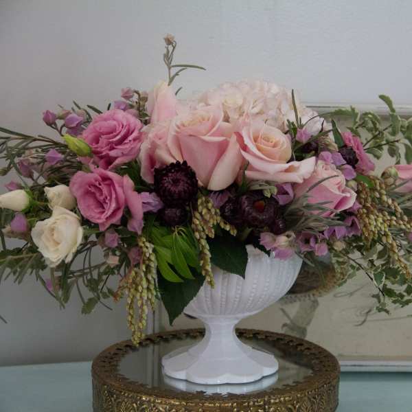 Pink and white rose arrangement in a white pedestal vase