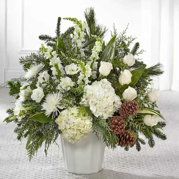 White floral arrangement in a white vase with pinecones and evergreen accents
