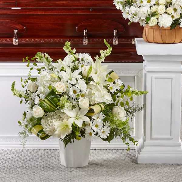 White floral arrangement in a vase beside a casket