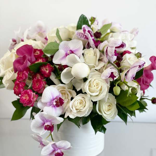 White and pink orchid and rose arrangement in a white vase