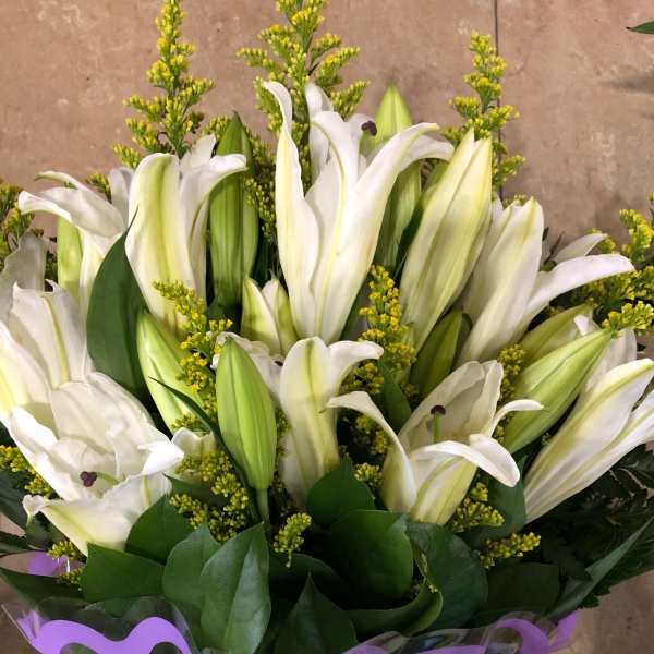 Bouquet of white lilies with yellow filler flowers and purple wrap