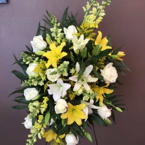 Standing floral spray with white roses and yellow lilies on a metal easel