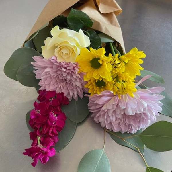 Bouquet of roses, chrysanthemums, and purple blooms wrapped in kraft paper