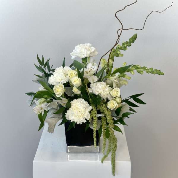 White carnations and roses arranged in a black square vase