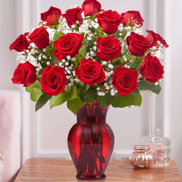 Arrangement of red roses with white filler flowers in a red glass vase on a wooden table