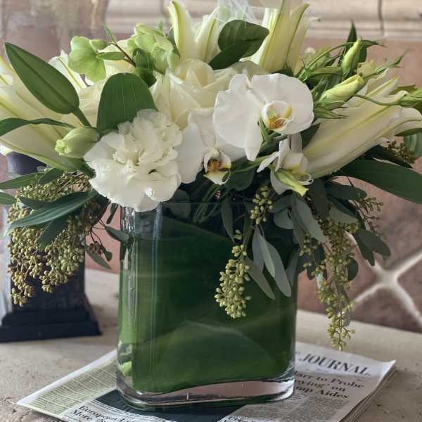 White floral arrangement in a glass vase with orchids and lilies