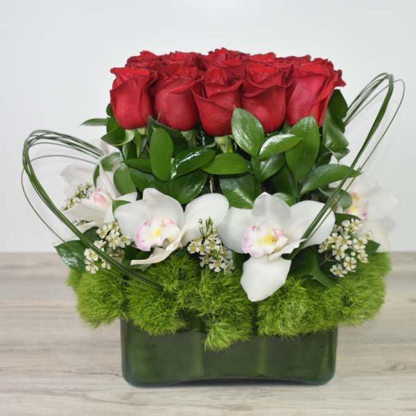 Compact arrangement of red roses, white orchids, and green dianthus in a rectangular green glass vase.