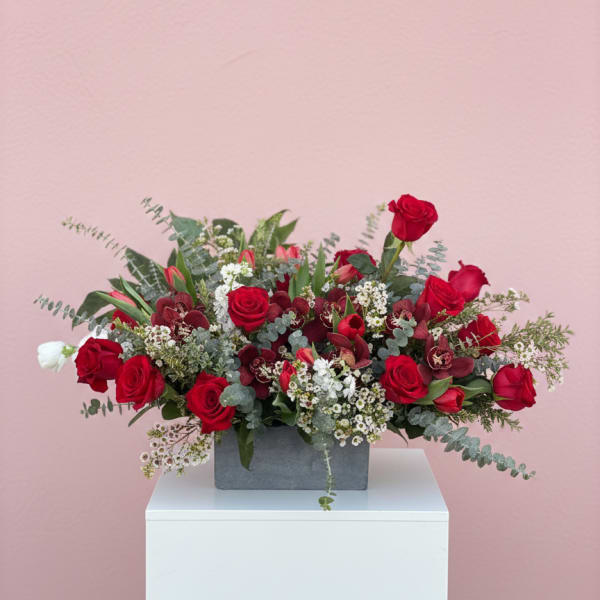 Red roses arranged in a gray rectangular vase with white filler flowers