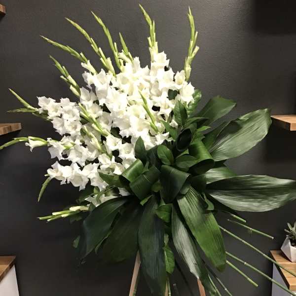 White gladiolus arrangement with large green leaves on an easel
