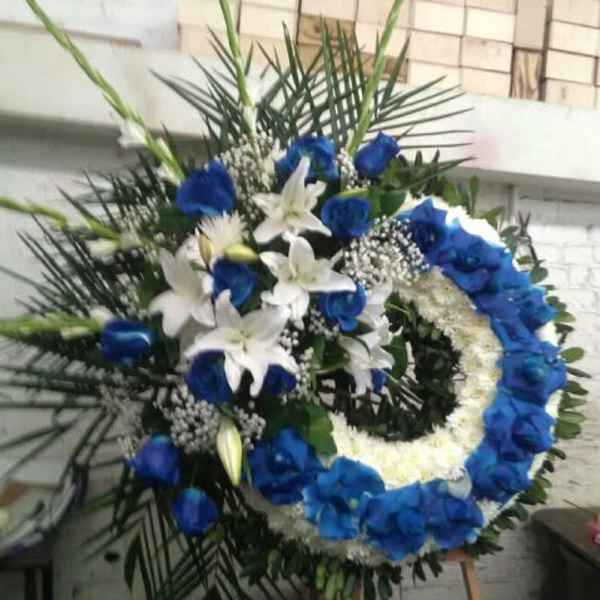 Standing wreath of blue roses and white lilies on a wooden easel.