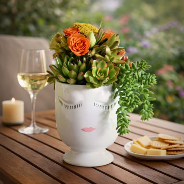 Succulent arrangement with orange roses in a white face vase