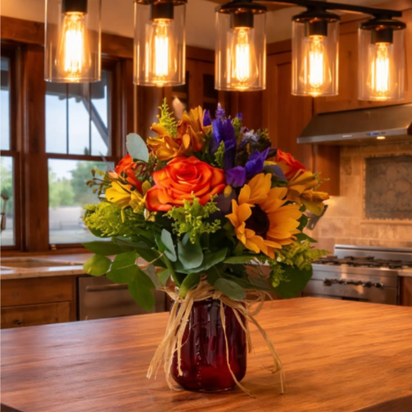 Bouquet of orange roses, sunflowers, and purple flowers in a red vase